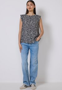 Top senza maniche con un motivo floreale blu navy e crema, con spalle arricciate. Abbinato a jeans a gamba larga blu chiaro e sneakers.