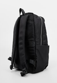 Černý nylonový batoh s polstrovanými ramenními popruhy, horním držadlem a boční kapsou. Má zapínání na zip a elegantní design.