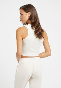 Bijeli rebrasti crop top s visokim izrezom i bez rukava, u kombinaciji sa svijetlosmešavim hlačama s elastičnim pojasom.