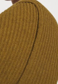 Ribbetty neulepusero lämpimässä sinapinvärissä, jossa on pehmeä tekstuuri ja pyöristetyt hartiat.