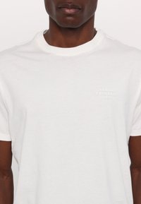 T-shirt en coton blanc avec un col rond et des manches courtes. Le logo "Armani Exchange 1991" est brodé sur la poitrine gauche.