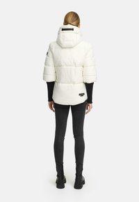Witte pufferjack met capuchon, korte mouwen en een vierkante snit. Voorzien van een logopatch aan de onderkant en een gestructureerd, doorgestikt oppervlak.