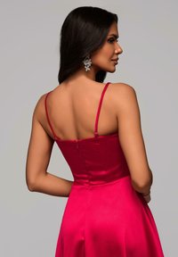 Robe satin fuchsia avec un corsage ajusté, des fines bretelles réglables et une fermeture éclair dissimulée au dos. Présente une jupe évasée.