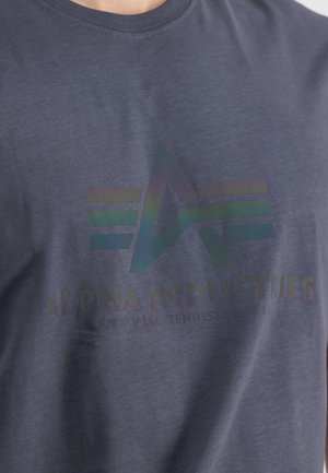 Navyblaue Baumwoll-T-Shirt mit einem glänzenden, schillernden Logo und dem Text "ALPHA INDUSTRIES, KNOXVILLE, TENNESSEE, USA" auf der Vorderseite.