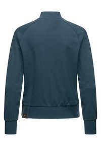 Felpa di un verde scuro con colletto alto, maniche raglan e polsini e orlo a coste. Presenta un piccolo etichetta di marca sul lato inferiore.
