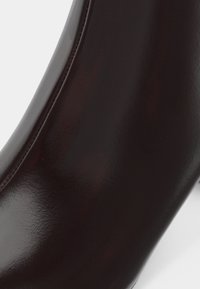 Detailní záběr na hladký tmavě hnědý kožený povrch s viditelnými švy na botě.