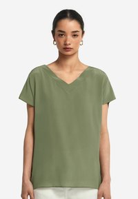V-ringad blus med korta ärmar i ljus olivgrön tyg, med en slät yta och avslappnad passform utan några ytterligare dekorationer.