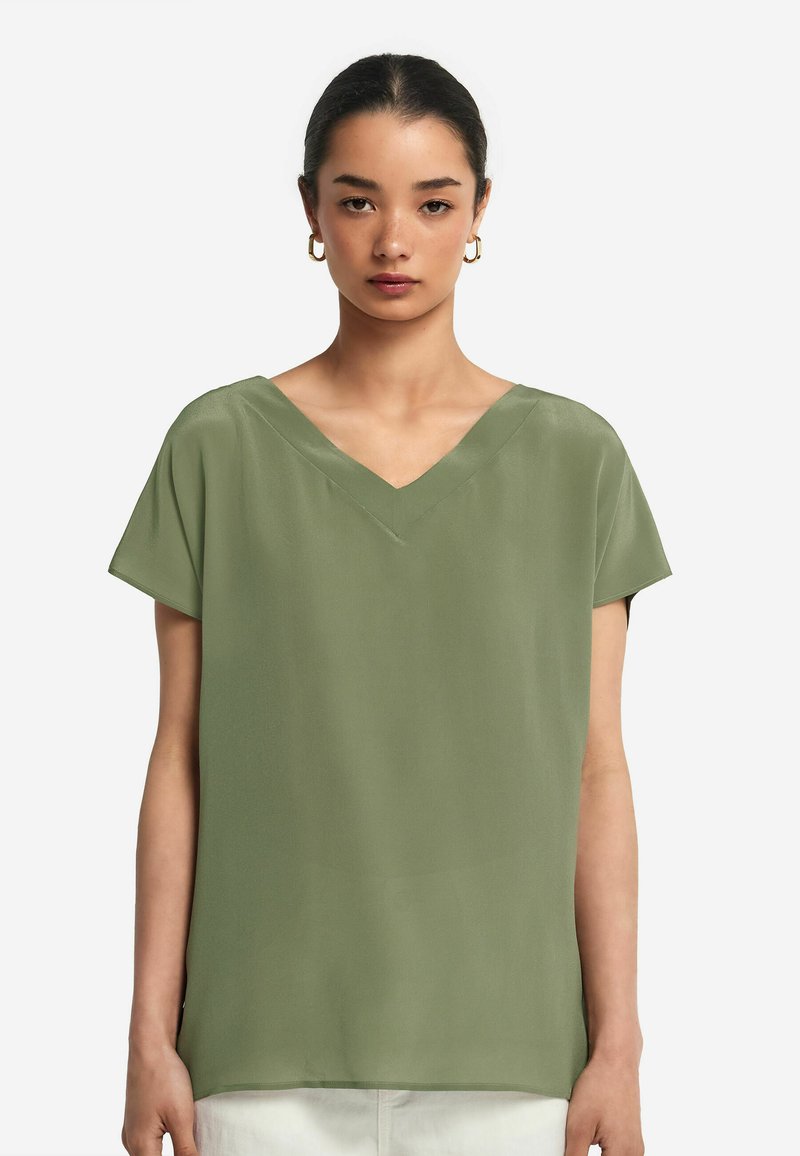 V-ringad blus med korta ärmar i ljus olivgrön tyg, med en slät yta och avslappnad passform utan några ytterligare dekorationer.