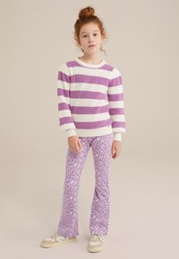 Maglione lavorato a maglia con righe bianche e lavanda, abbinato a pantaloni a campana lavanda con un motivo floreale. Le sneakers completano l'outfit.