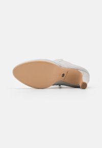 Gray suede shoe with a rounded toe and a low, tan rubber heel. The outsole features a smooth texture and a stylish logo imprint.