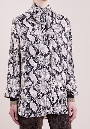 Blouse à manches longues avec imprimé serpent noir et blanc et foulard noué au cou, portée sur un pantalon scintillant.