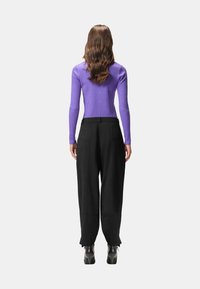 Top viola a costine a maniche lunghe abbinato a pantaloni neri a gamba larga a vita alta e stivali neri con tacco, visto da dietro.