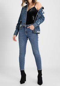 Džínsová bunda s opotřebovanými detaily, černý přiléhavý top s květinovou výšivkou a modré skinny džíny doplněné černými vysokými botami na podpatku.