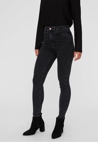 Jeans skinny negros de cintura alta hechos de denim, con una textura suave y un cierre delantero de botón, combinados con botas de tobillo negras.