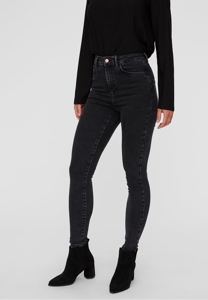 Jeans skinny negros de cintura alta hechos de denim, con una textura suave y un cierre delantero de botón, combinados con botas de tobillo negras.