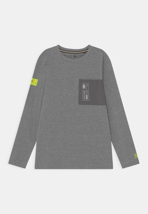 Camiseta de manga larga gris con bolsillo en el pecho de color gris oscuro que presenta texto blanco y etiquetas de color amarillo neón en la manga izquierda y la muñeca derecha.