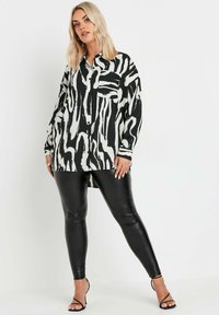 Black and white abstract-patterned button-up shirt with long sleeves, paired with black shiny leggings and strappy heels.