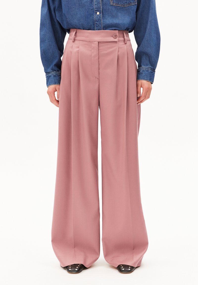 Lichtroze wijde broek met een hoge taille, voorzien van plooien, een knoopsluiting, en gecombineerd met een denim shirt en zwarte puntige schoenen.