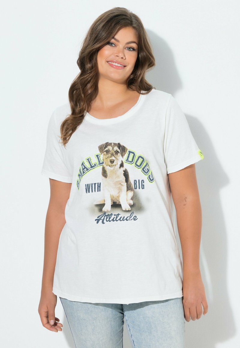 Kobieta o falujących brązowych włosach, ubrana w białą koszulkę z małą ilustracją psa i napisem "Małe psy z wielką osobowością".
