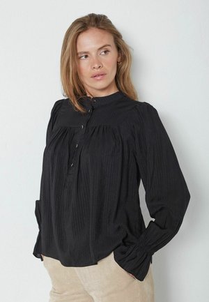 Bluză neagră cu guler în picioare, față pliată și închidere cu nasturi. Fabricată dintr-un material ușor, cu dungi texturate subtile și mâneci lungi.