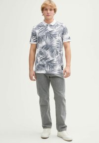 Biała koszulka polo z krótkim rękawem w czarny wzór liści, zestawiona z jasnoszarymi dżinsami i białymi trampkami. Casualowy krój i gładka tekstura.