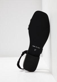 Sandale noire avec une semelle texturée. Fabriquée en Italie, taille 37, elle présente un design simple et une bride à la cheville. Matériau lisse avec des accents minimalistes.