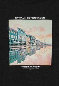 Černé tričko s potiskem zobrazujícím přístav Nyhavn v Kodani, s barevnými budovami odrážejícími se ve vodě při západu slunce. Text nahoře a dole.