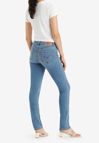 Ljusblå denimjeans med en figursydd design, med bakfickor och en läderetikett i brunt. Tillsammans med en vit topp med kort ärm och sandaler.