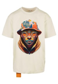 Krémové tričko s živým grafickým potlačou tváre v multikolórovom vedierkovom klobúku a oranžovej zip-up mikine.