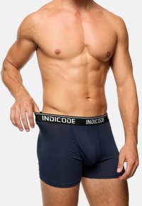 Marineblaue Boxershorts aus einem weichen Stoff, mit einem schwarzen elastischen Bund, der das "INDICODE"-Logo in weißer Schrift trägt.