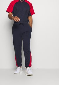 Survêtement sportif bleu marine et rouge à manches courtes, taille élastique, poches latérales et détails de panneaux rouges contrastants sur le pantalon.