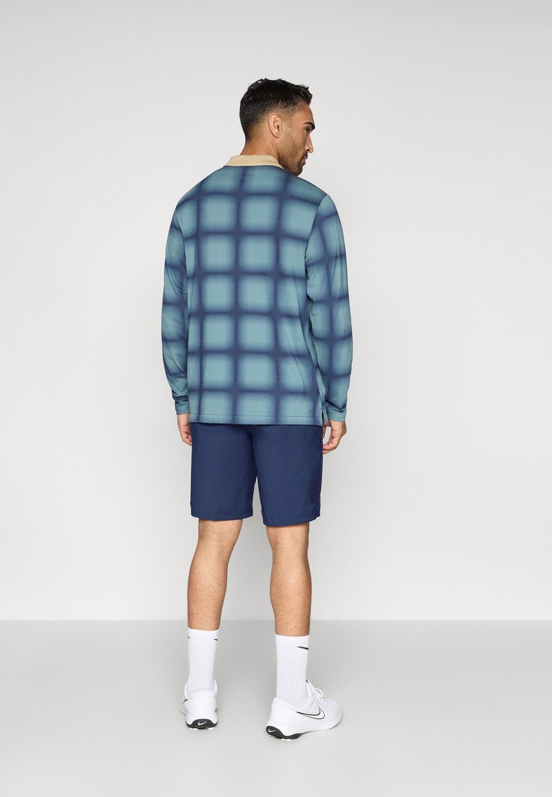 Langärmliges Shirt in verlaufendem Türkis mit Karomuster, kombiniert mit navyblauen Shorts. Baumwollmischung, lockere Passform, Kragen und keine sichtbaren Logos.