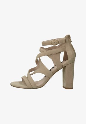 Beige suede hoge hak sandaal met kruislings banden, verstelbare enkelband met gouden gesp en een stevige blokhak.