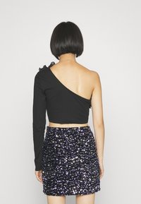 Mustassa ribatulla cropped-paita, jossa on yksi pitkä hiha ja rypytys; yhdistettynä paljettimekkoiseen violettiin ja mustaan mini-hameeseen, jossa on kiiltäviä koristeita.