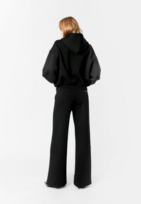 Sudadera negra de gran tamaño con capucha, combinada con pantalones de cintura alta y pierna ancha negros. Tejido suave con un diseño casual.