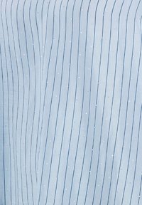 Lichtblauwe stof met verticale strepen en kleine zilveren stippen. Het materiaal lijkt zacht met een lichte glans en heeft een gladde textuur.