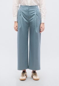 Lichtblauwe wijde broek met voorvouwen, gladde textuur, hoge taille, gecombineerd met beige en zwarte sneakers.