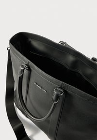 Černá kožená taška přes rameno s texturovaným povrchem, vybavená dvojitými uchy a odnímatelným popruhem. Uvnitř se nachází zipová kapsa a branding.