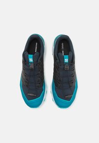 Scarpe da corsa con una tomaia blu navy, dettagli neri, suola turchese e sistema di allacciatura, realizzate con un tessuto testurizzato per supporto e comfort.