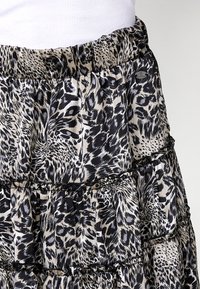Jupe imprimée animalière noire et beige avec un design en étages, dotée d'une taille élastique et de détails en dentelle subtils. Tissu texturé.