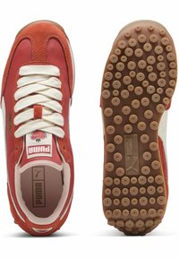 Piros velúr és szövet sneaker fehér fűzőkkel, gumi pöttyös talppal, valamint Puma márkázással a nyelvén és a sarkán.