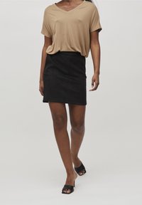 Beige, V-čkový, volný top spárovaný s černou, přiléhavou minisukní. Model má na sobě černé muly s otevřenou špičkou. Příjemná textilní struktura po celé ploše.