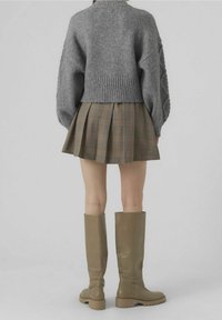 Grijze gebreide trui, geruite plissé rok en beige laarzen tot de knie. De trui heeft een cropped pasvorm en tekstuurslouwen. De laarzen hebben een stevige zool.