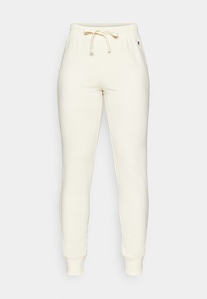 Pantaloni de trening crem, cu un brâu elastic și șnur, având mansete ribbate și un logo mic pe lateral. Textură moale și netedă.
