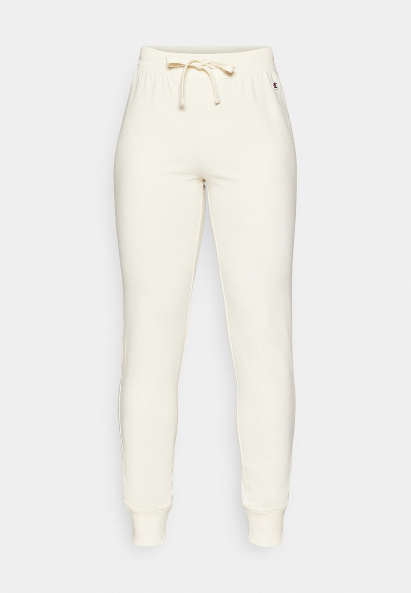 Pantalones deportivos de color crema con cinta elástica en la cintura y cordón, con puños acanalados y un pequeño logotipo en el lado. Textura suave y lisa.