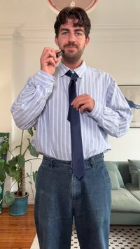 Šviesiai mėlyna ir balta raišteliu apririšta marškiniai su dryžiais, derinami su tamsiai mėlynu kaklaraiščiu. Dėvimi tamsios džinsinės kelnės. Asmuo laiko juodą objektą.