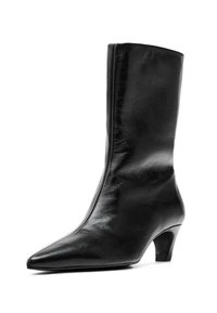 Bottine en cuir noir avec un bout pointu, texture lisse et un talon de hauteur intermédiaire, affichant une silhouette épurée et minimaliste.