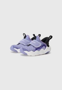 Des chaussures de sport violettes avec un dessus en tricot texturé, une semelle ondulée blanche, et une sangle en velcro ajustable, comportant un talon noir et des accents de logo.