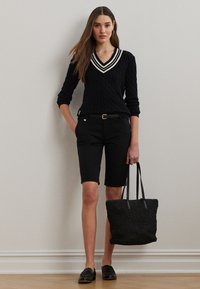 Adīts melns džemperis ar baltām V formas kakla svītrām, melnas pielāgotas šortas, melnas loaferu kurpes un melna teksturēta tote soma.