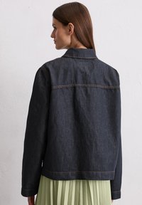Dark denim jacket with a collar, visible stitching, and a relaxed fit, paired with a pleated light green skirt.